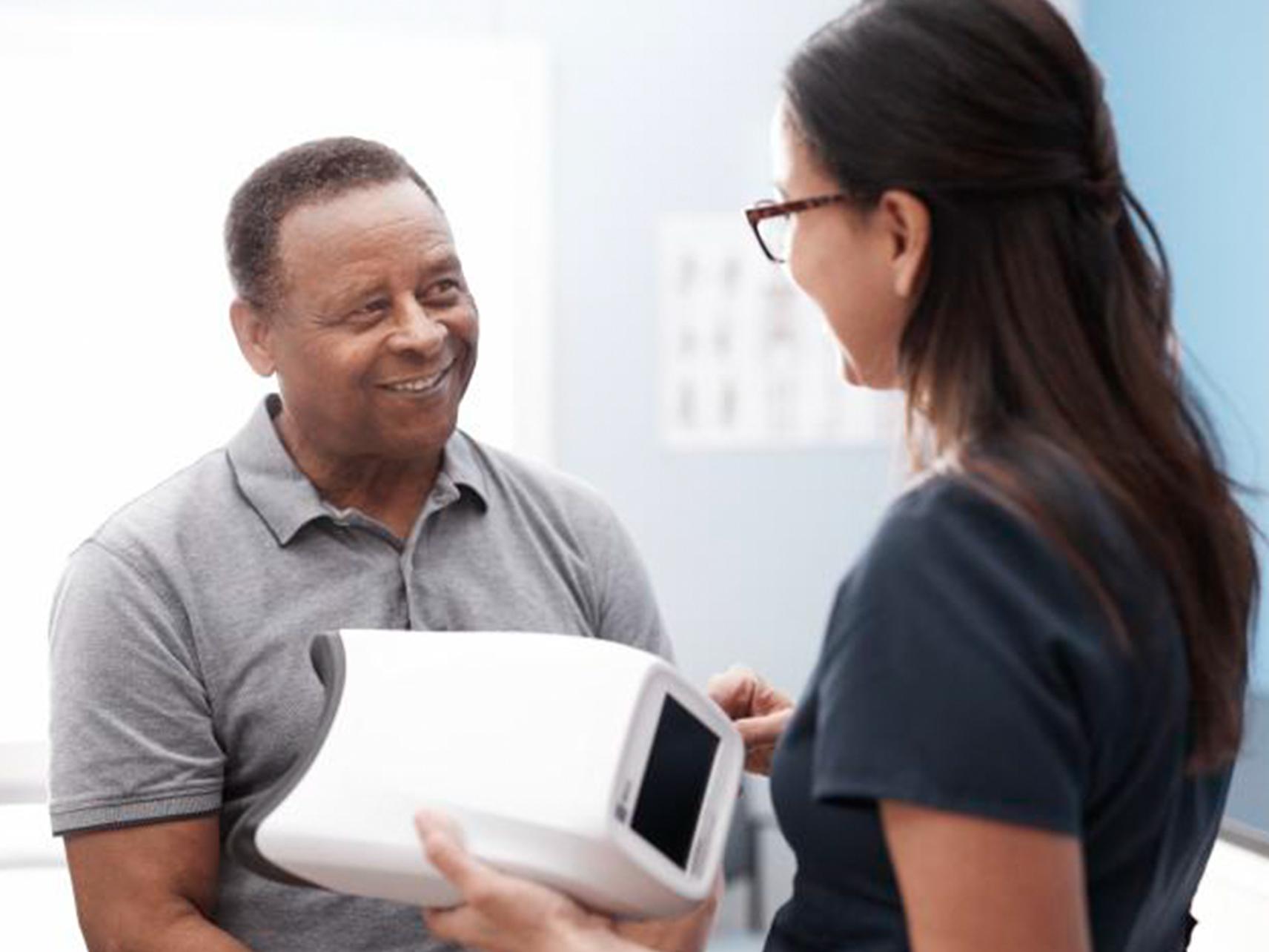 A patient and caregiver with a Welch Allyn® RetinaVue® 700 Imager in her hand, smile at each other.